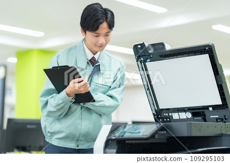 A young male worker maintaining a copy machine in an office A young male worker maintaining a copy machine in an office 109295103