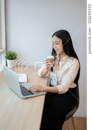 Beautiful Asian businesswoman is having a morning coffee while working on her laptop in the office. 109295450