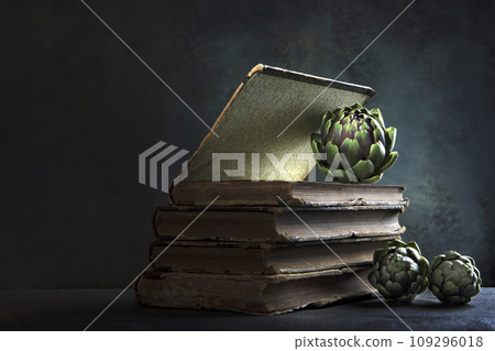 The artichokes are on the book. Artichokes and an old book. Dark background. An old book. Copy space. 109296018