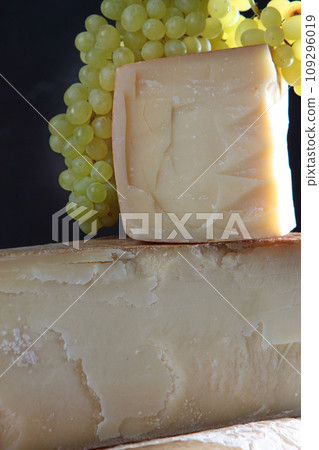 A bunch of grapes and cheeses. Large chunks of hard cheese. Hard cheeses. 109296019