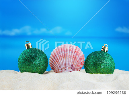 Pink conch with Christmas shiny green balls on sand of beach with sea. New Year, holiday. Copy space 109296288