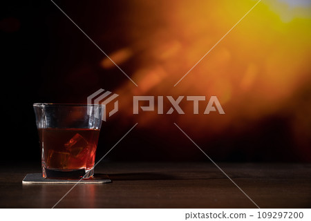 Glass of whiskey on the bar in front of the blur image Abstract Natural Sun flare on the black Glass of whiskey on the bar in front of the blur image Abstract Natural Sun flare on the black 109297200