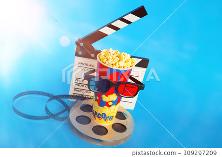 Movie clapper, pop corn, 3D glasses and film reel on blue background. Collage design Movie clapper, pop corn, 3D glasses and film reel on blue background. Collage design 109297209
