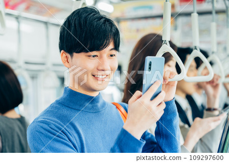 A college student looking at a smartphone on a train. Photo provided by Keio Electric Railway Co., Ltd. 109297600
