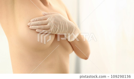Naked woman examines breasts in gloved hands 109298136
