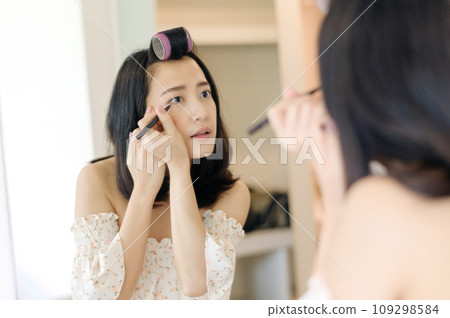 Beautiful young Asian woman applying makeup in front of the mirror. Lifestyle people concept. Advertisement for skin cream, anti-wrinkle cream, baby face 109298584