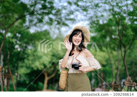 Portrait of asian young woman traveler with weaving hat and basket and a camera on green public park nature background. Journey trip lifestyle, world travel explorer or Asia summer tourism concept. Portrait of asian young woman traveler with weaving hat and basket and a camera on green public park nature background. Journey trip lifestyle, world travel explorer or Asia summer tourism concept. 109298614