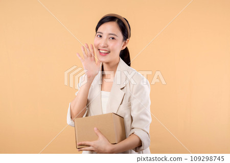 portrait of happy successful confident young asian business woman wearing white jacket holding parcel box isolated on beige studio background, Delivery courier and shipping service concept. 109298745