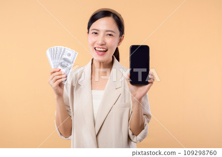 portrait of happy successful confident young asian business woman wearing white jacket holding smartphone and cash money dollar standing over beige background. millionaire business, shopping concept. 109298760