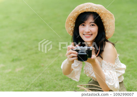 Portrait of asian young woman traveler with weaving hat and basket and a camera on green public park nature background. Journey trip lifestyle, world travel explorer or Asia summer tourism concept. Portrait of asian young woman traveler with weaving hat and basket and a camera on green public park nature background. Journey trip lifestyle, world travel explorer or Asia summer tourism concept. 109299007