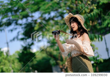 Portrait of asian young woman traveler with weaving hat and basket and a camera on green public park nature background. Journey trip lifestyle, world travel explorer or Asia summer tourism concept. Portrait of asian young woman traveler with weaving hat and basket and a camera on green public park nature background. Journey trip lifestyle, world travel explorer or Asia summer tourism concept. 109299030