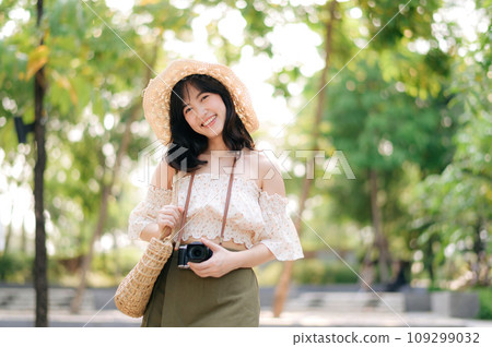 Portrait of asian young woman traveler with weaving hat and basket and a camera on green public park nature background. Journey trip lifestyle, world travel explorer or Asia summer tourism concept. 109299032