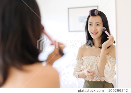 Beautiful young Asian woman applying makeup in front of the mirror. Lifestyle people concept. Advertisement for skin cream, anti-wrinkle cream, baby face Beautiful young Asian woman applying makeup in front of the mirror. Lifestyle people concept. Advertisement for skin cream, anti-wrinkle cream, baby face 109299242