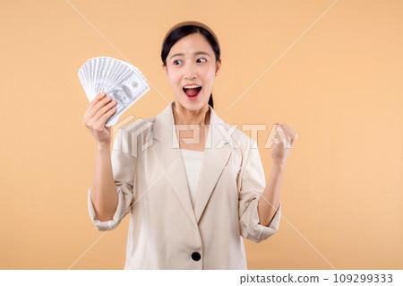 portrait of happy successful confident young asian business woman wearing white jacket holding cash money dollars standing over beige background. millionaire business, shopping concept. portrait of happy successful confident young asian business woman wearing white jacket holding cash money dollars standing over beige background. millionaire business, shopping concept. 109299333