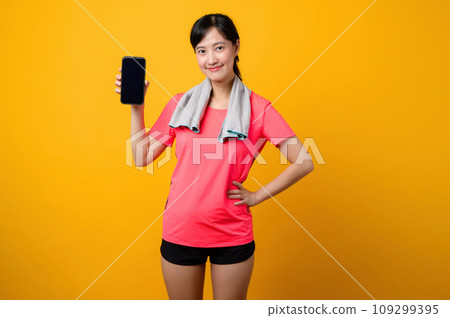 Portrait young asian sports fitness woman happy smile wearing pink sportswear and smartphone doing exercise training workout against yellow studio background. technology wellness lifestyle concept. Portrait young asian sports fitness woman happy smile wearing pink sportswear and smartphone doing exercise training workout against yellow studio background. technology wellness lifestyle concept. 109299395