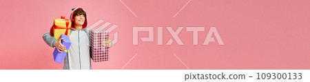 Banner. Charming young man standing and holds a lot of presents against pink background with negative space for text. Banner. Charming young man standing and holds a lot of presents against pink background with negative space for text. 109300133