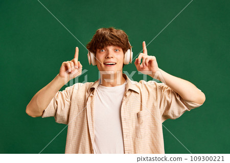 Portrait of cheerful handsome man stands raising hand and pointing that he have new idea or answer against green studio background. 109300221