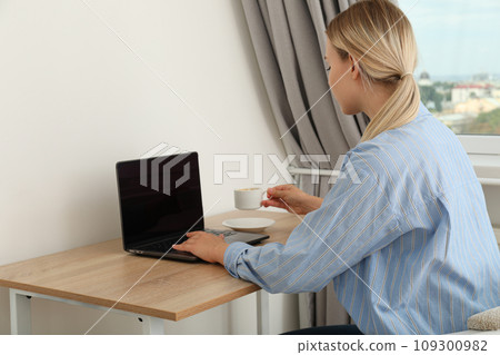 A woman with a cup of coffee is working on a laptop A woman with a cup of coffee is working on a laptop 109300982