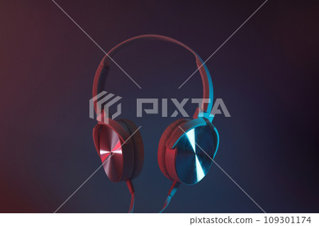 White, over-the-ear headphones with a wire on a colored, dark background. 109301174
