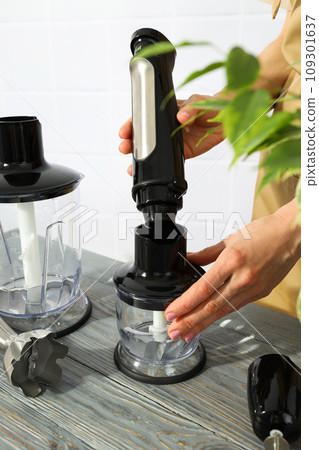 Black blender with attachments in hands on wooden table on white background Black blender with attachments in hands on wooden table on white background 109301637