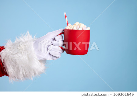Cup with marshmallows in Santa's hand on blue background 109301649