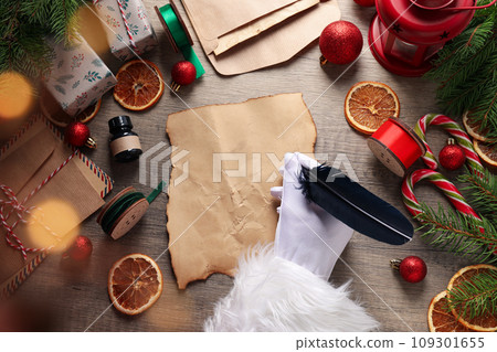 Gift boxes, letters, vintage paper and feather in Santa's hand on wooden background, top view Gift boxes, letters, vintage paper and feather in Santa's hand on wooden background, top view 109301655