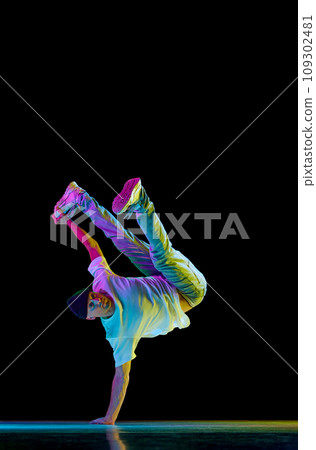 Dance show. Athletic guy dancing contemp, breakdance and hip-hop against black studio background in mixed neon light. 109302481
