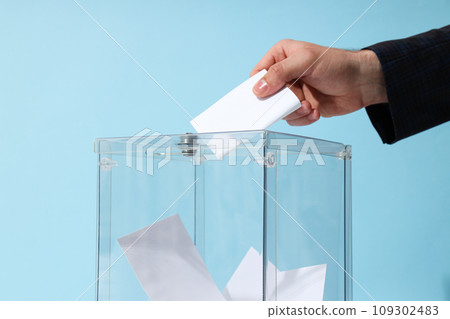 Voting box with papers and hand on blue background, close up 109302483