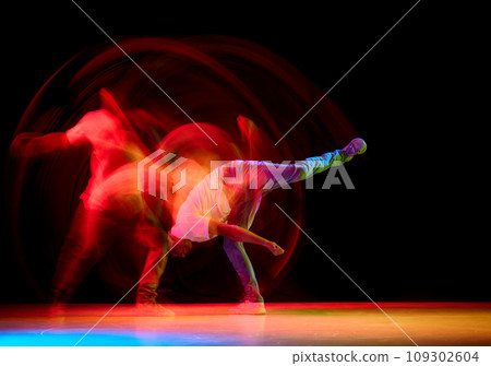 Young sportive guy dancing hip-hop, breakdance against black studio studio background in red neon light with motion blur. 109302604