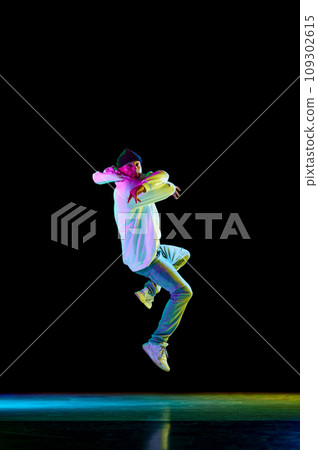 Modern dance. Breakdance male dancer, athletic guy dancing freestyle in stylish outfit against black background in neon light. 109302615