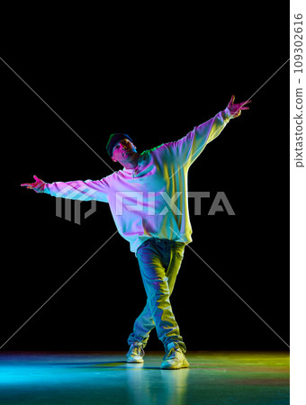 Hey-yo. Modern dance. Breakdance male dancer, athletic guy dancing freestyle in stylish outfit against black background in neon light. Hey-yo. Modern dance. Breakdance male dancer, athletic guy dancing freestyle in stylish outfit against black background in neon light. 109302616