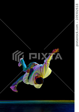 Sportive b-boy dancing hip-hop in stylish clothes against black background at dance hall in neon light, filter. In motion, action. Sportive b-boy dancing hip-hop in stylish clothes against black background at dance hall in neon light, filter. In motion, action. 109302618