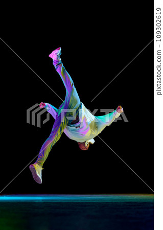 Sportive b-boy dancing hip-hop in stylish clothes against black background at dance hall in neon light, filter. 109302619