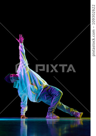 Young sportive guy dancing hip-hop, breakdance against black studio studio background in mixed colorful neon light. Young sportive guy dancing hip-hop, breakdance against black studio studio background in mixed colorful neon light. 109302622