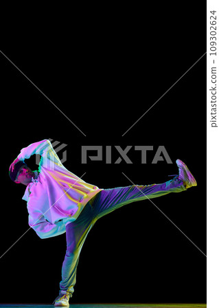 Full-length portrait of hip-hop male dancer, athletic guy dancing in stylish outfit against black background in mixed neon light. 109302624