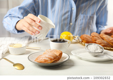 Madeleine cakes, butter, flour and milk jug in hand on light background 109302832