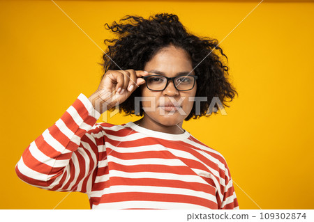 Curly young woman in glasses on yellow background Curly young woman in glasses on yellow background 109302874