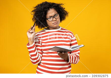 Curly young woman in glasses with book in hand on yellow background Curly young woman in glasses with book in hand on yellow background 109302875