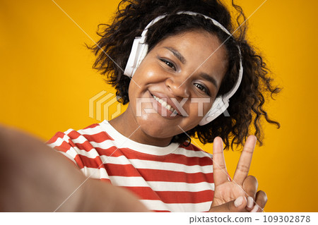 Selfie of curly young woman with headphones on yellow background 109302878