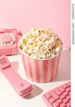 Popcorn in paper cup, keyboard and phone on pink background 109303241