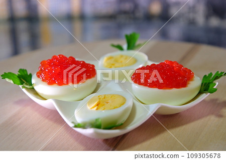 Put black caviar on an egg to serve delicious healthy food Halves of a hard-boiled chicken egg with red caviar on a wooden background. Put black caviar on an egg to serve delicious healthy food Halves of a hard-boiled chicken egg with red caviar on a wooden background. 109305678