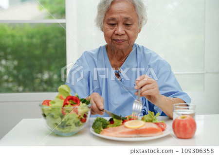 Asian elderly woman patient eating salmon stake and vegetable salad for healthy food in hospital. Asian elderly woman patient eating salmon stake and vegetable salad for healthy food in hospital. 109306358
