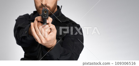 Looking down barrel of anonymous police officer's sidearm in studio. Crop view of unrecognizable constable aiming, by pointing handgun to camera, isolated on gray. Concept of danger, work, weapon. Looking down barrel of anonymous police officer's sidearm in studio. Crop view of unrecognizable constable aiming, by pointing handgun to camera, isolated on gray. Concept of danger, work, weapon. 109306516