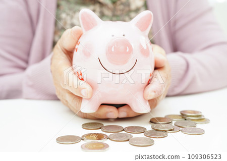 Retired elderly woman counting coins money with piggy bank and worry about monthly expenses and treatment fee payment. Retired elderly woman counting coins money with piggy bank and worry about monthly expenses and treatment fee payment. 109306523
