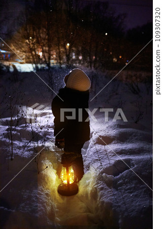 A little boy stands and looks at flying snowflakes. Winter evening. 109307320