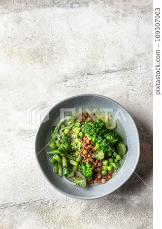 Vegetarian minestrone soup with green vegetables and lentils in gray plate on textured background with text space, top view 109307903