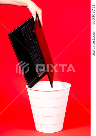Black laptop in a trash bin on a red background isolated 109308711