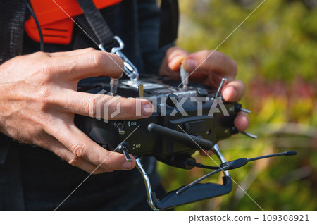 Close-up of a man's hands holding a transmitter and control equipment for an FPV drone quadcopter. Drone control concept Close-up of a man's hands holding a transmitter and control equipment for an FPV drone quadcopter. Drone control concept 109308921