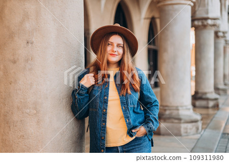 Attractive young female tourist is exploring new city. Redhead girl in hat posing on Market Square in Krakow. Traveling Europe in autumn. High quality photo, The Cloth Hall. Vacation concept Attractive young female tourist is exploring new city. Redhead girl in hat posing on Market Square in Krakow. Traveling Europe in autumn. High quality photo, The Cloth Hall. Vacation concept 109311980