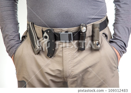 folding knife and a flashlight with clips on the belt of a tourist trekking trousers. EDC items folding knife and a flashlight with clips on the belt of a tourist trekking trousers. EDC items 109312483